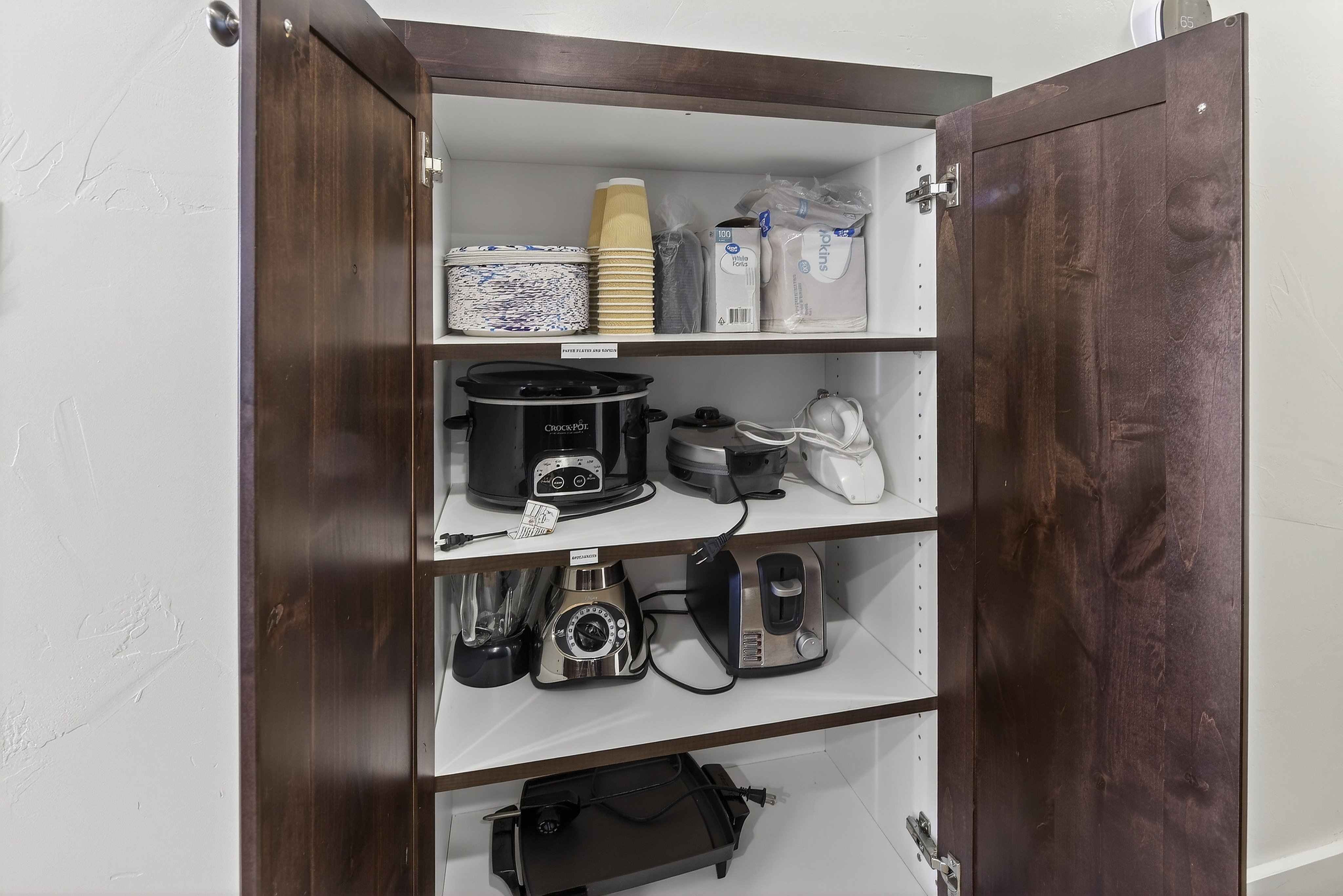 Built-in pantry cabinet featuring rich wood-finish doors, interior shelving, and a bright white interior finish
