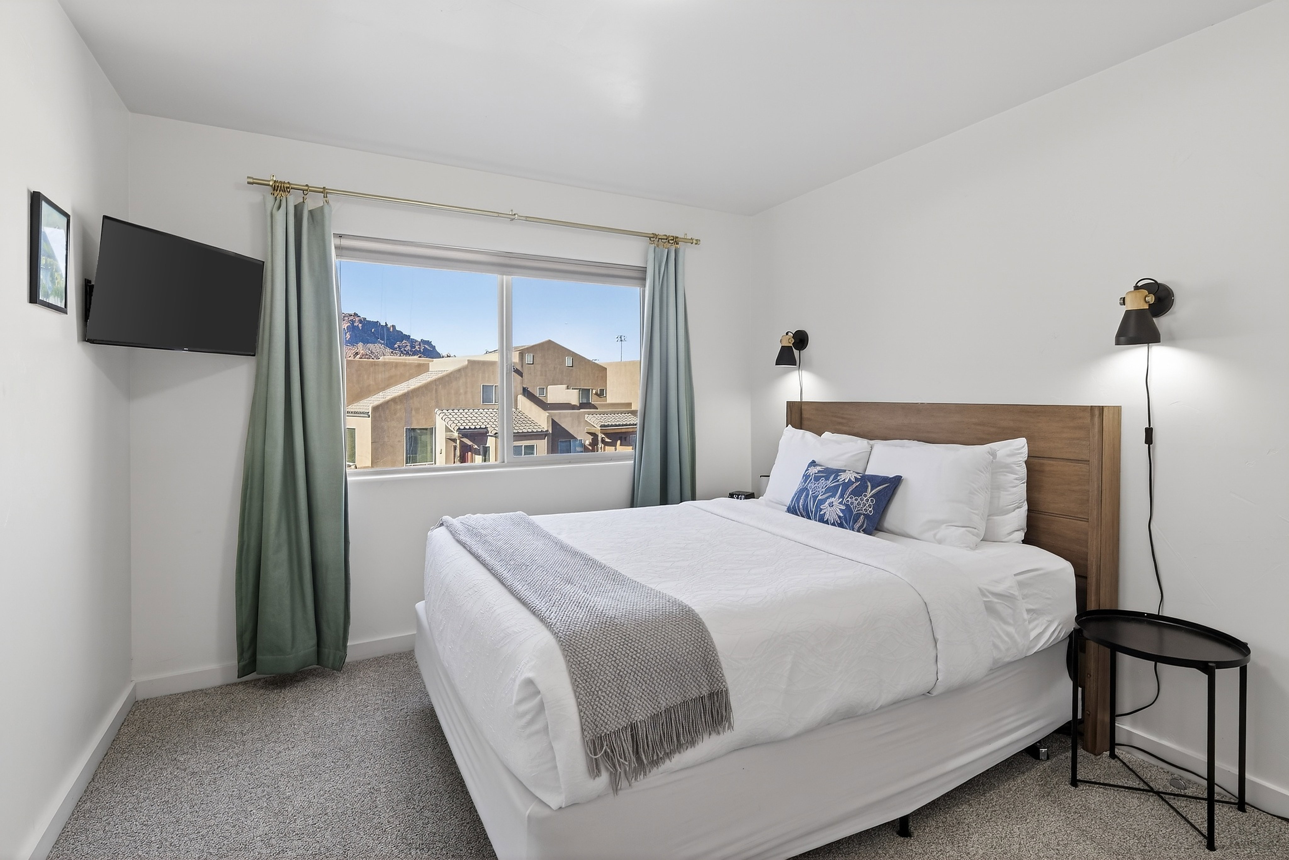 Bedroom featuring a large window, wall-mounted television, and sconce lighting