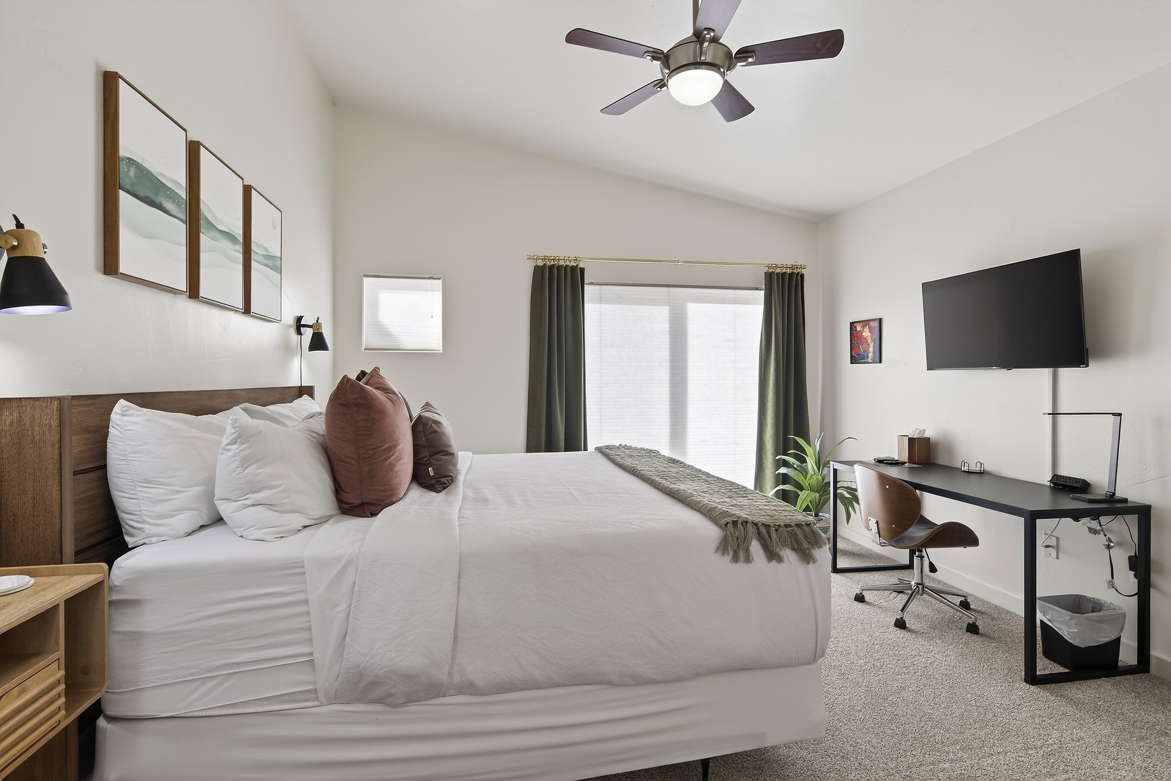 Vaulted ceiling bedroom featuring a wood-finish headboard, a ceiling fan with light fixture, wall-mounted sconces, and a large window with privacy blinds