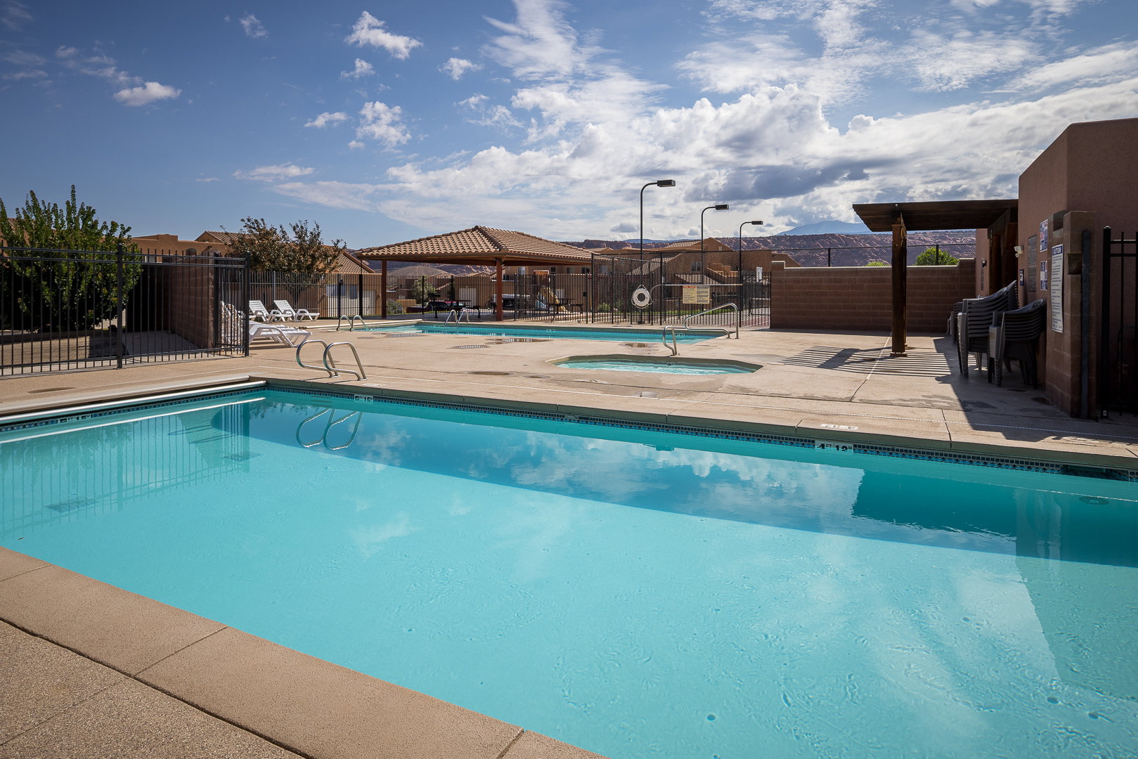 Outdoor swimming pool with surrounding concrete decking, a hot tub, and a shaded pergola area