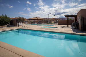 Outdoor swimming pool with surrounding concrete decking, a hot tub, and a shaded pergola area
