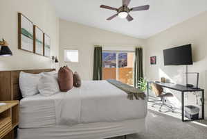 Bedroom featuring a vaulted ceiling with a ceiling fan, wood-finish headboard, built-in sconce lighting, and a sliding glass door