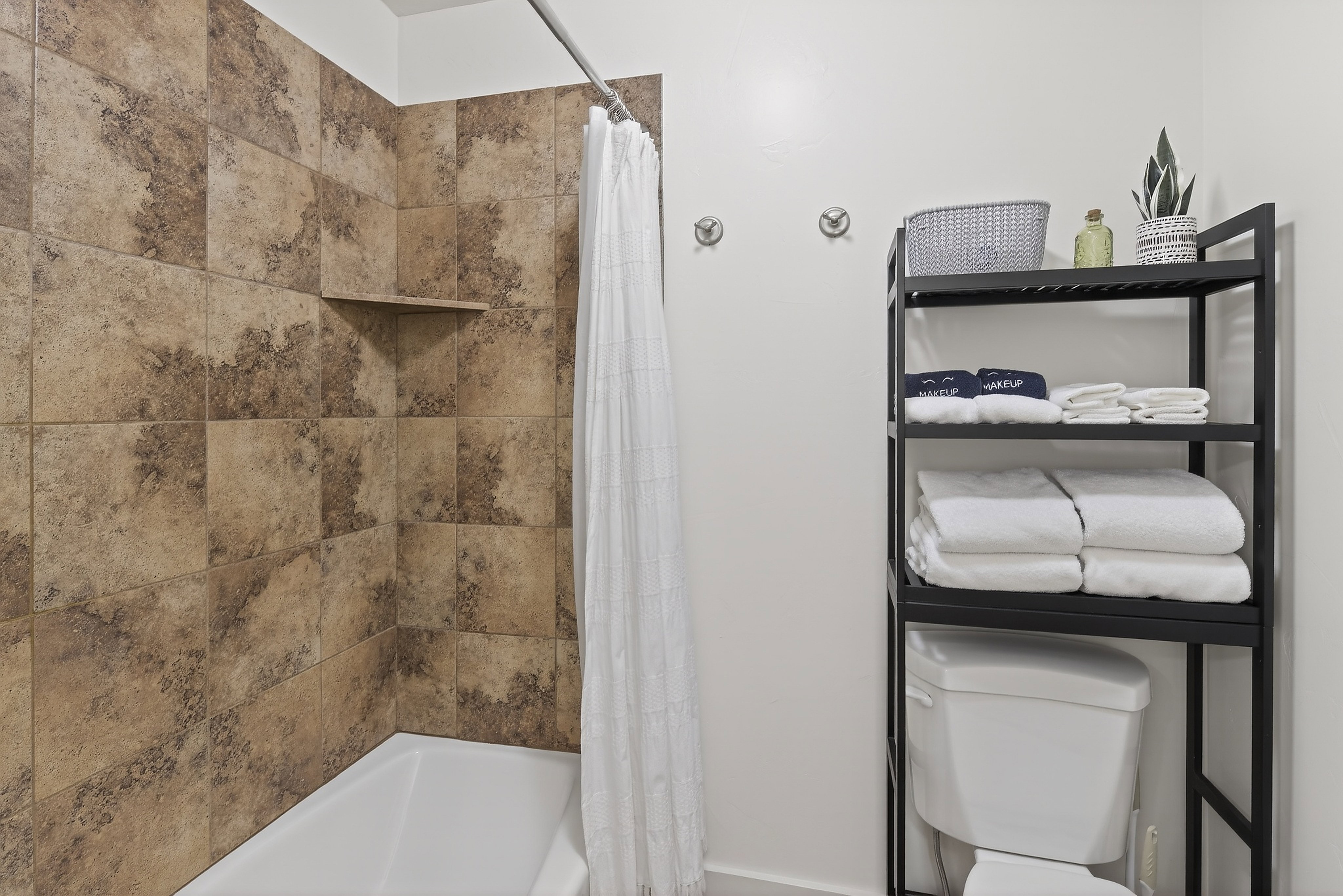 Bathtub with a tiled surround featuring a built-in shower shelf, complemented by a white shower curtain and a chrome shower rod