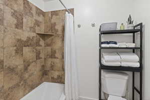 Bathtub with a tiled surround featuring a built-in shower shelf, complemented by a white shower curtain and a chrome shower rod