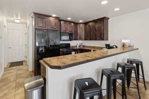 Kitchen with dark wood-finish cabinetry, black appliances, and stone-finish countertops