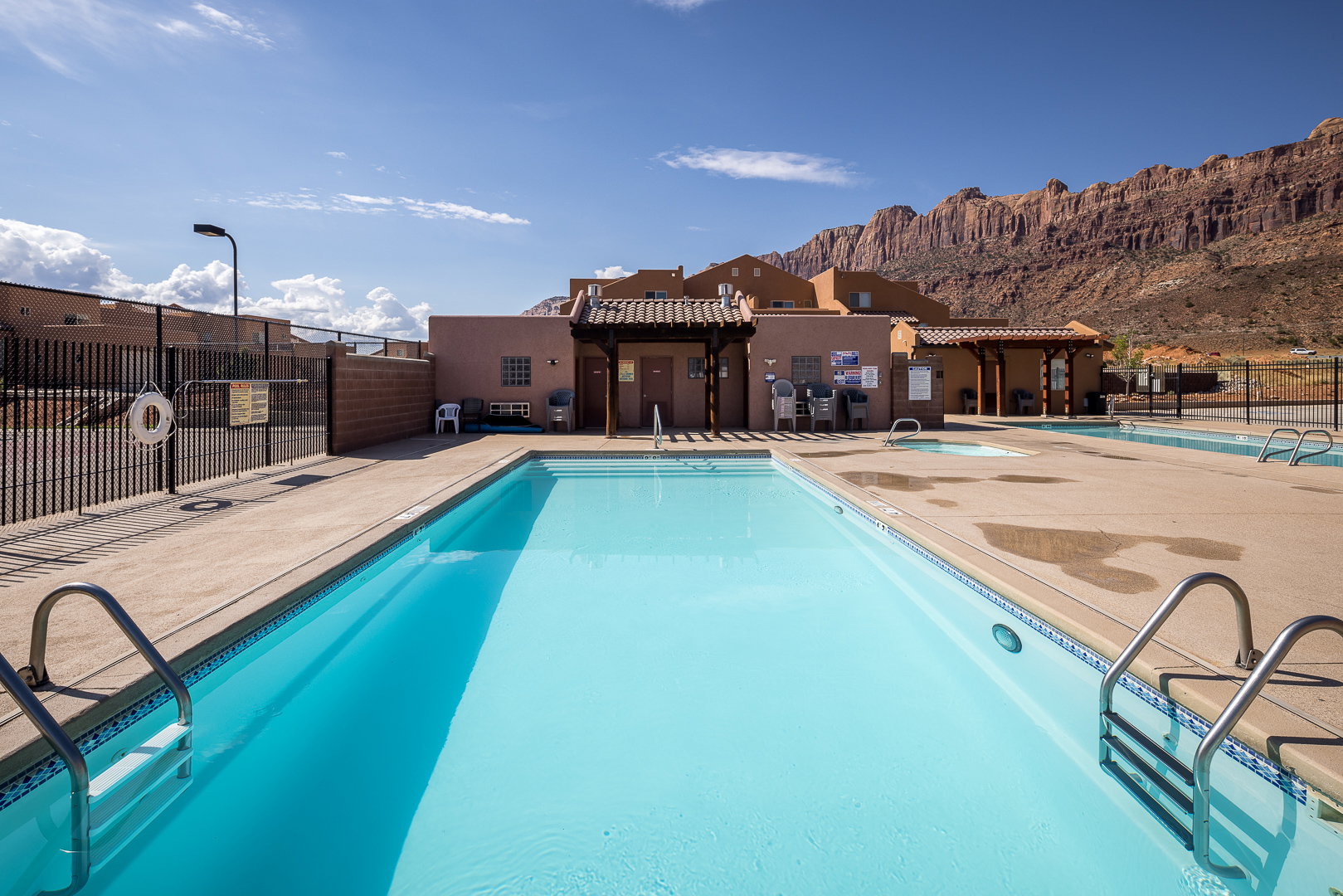 Resort-style pool area with ample concrete decking, stainless steel pool ladders, and a decorative tile border