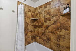 Tub and shower combination featuring earth-toned tile surround with integrated shelving