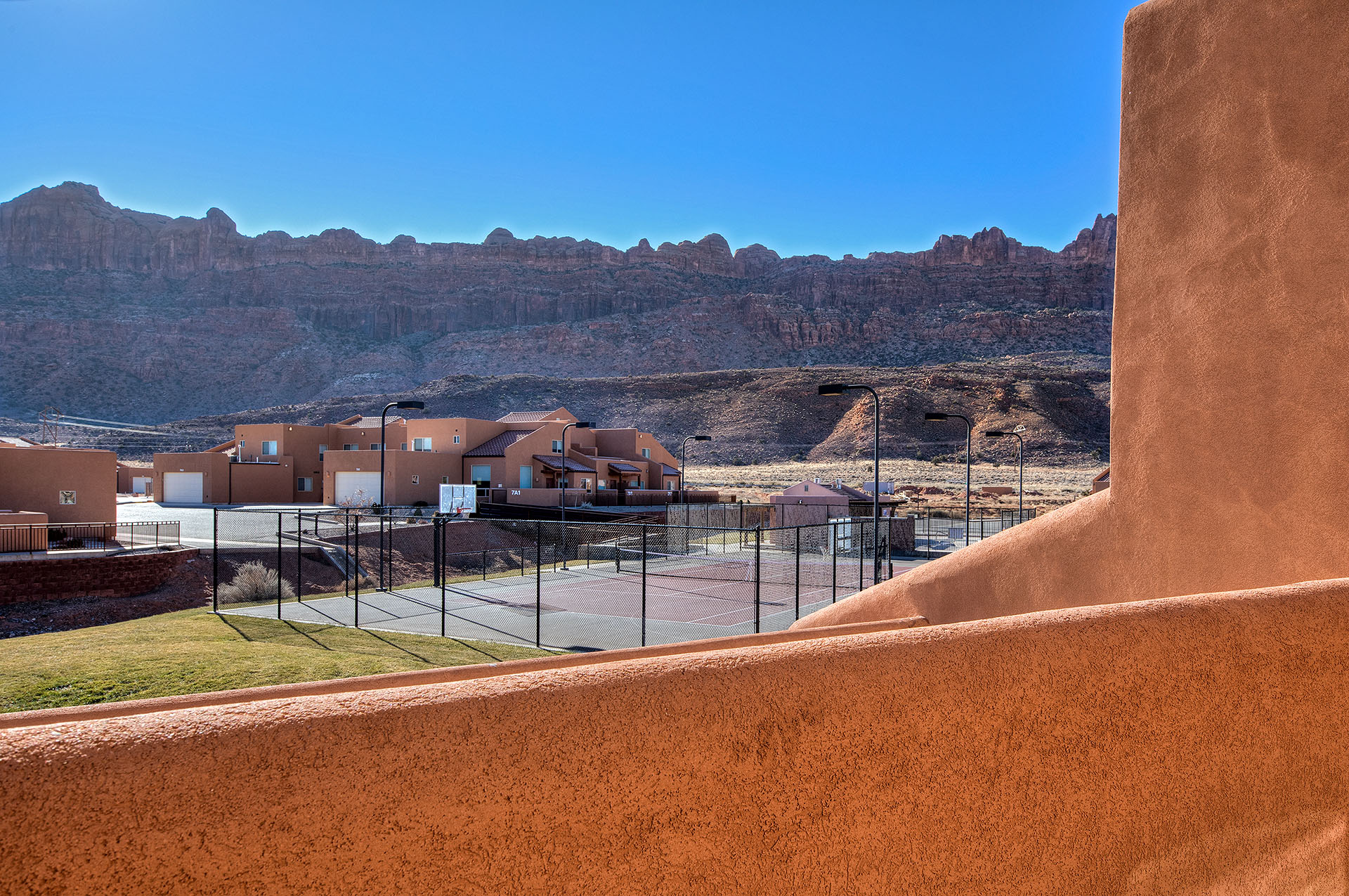 Outdoor sports court with fencing, surrounded by stucco residential structures featuring attached garages