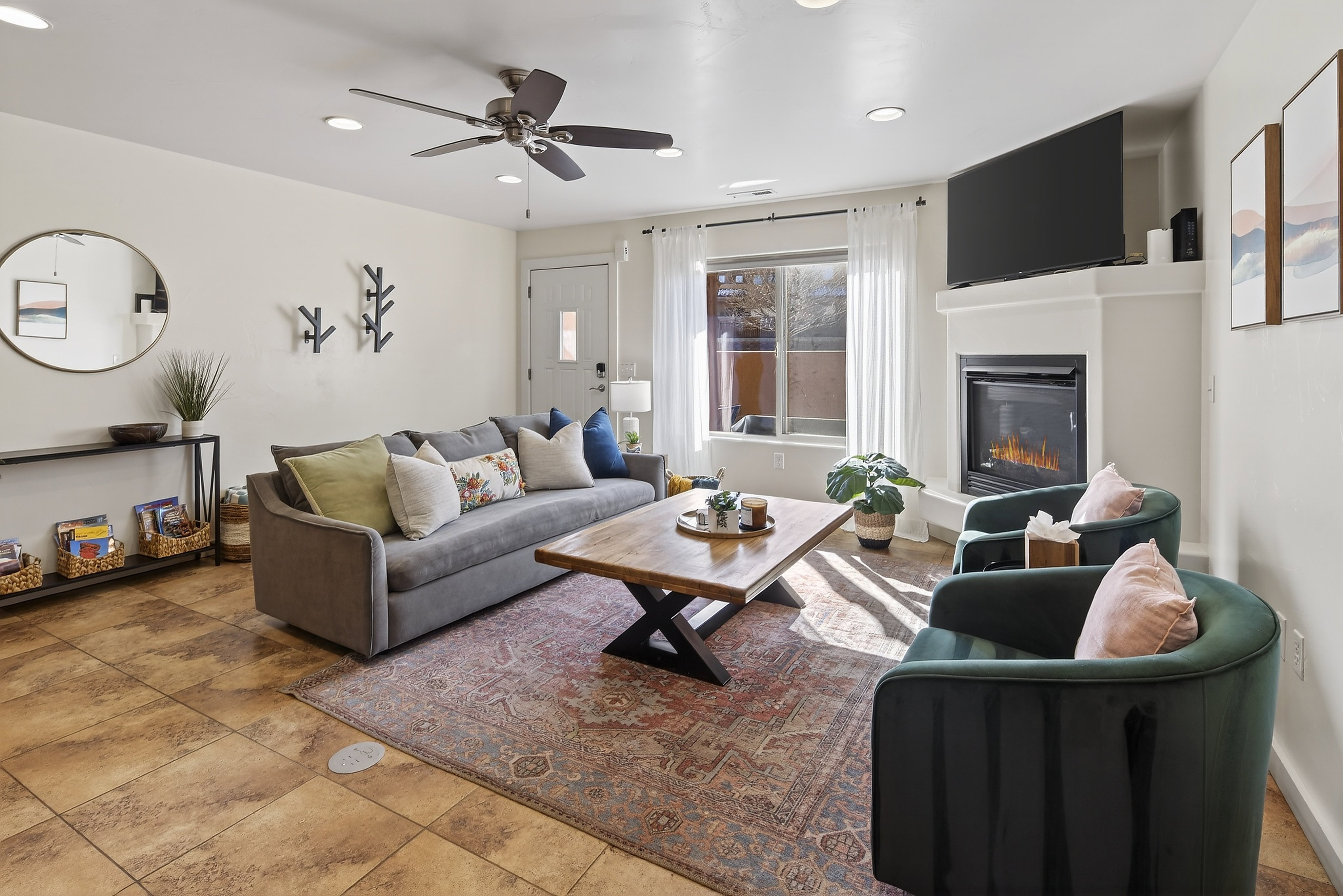 Living area featuring tile flooring, a corner fireplace with a mounted television, a large window with white sheer curtains, and recessed ceiling lighting