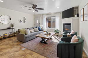 Living area featuring tile flooring, a corner fireplace with a mounted television, a large window with white sheer curtains, and recessed ceiling lighting