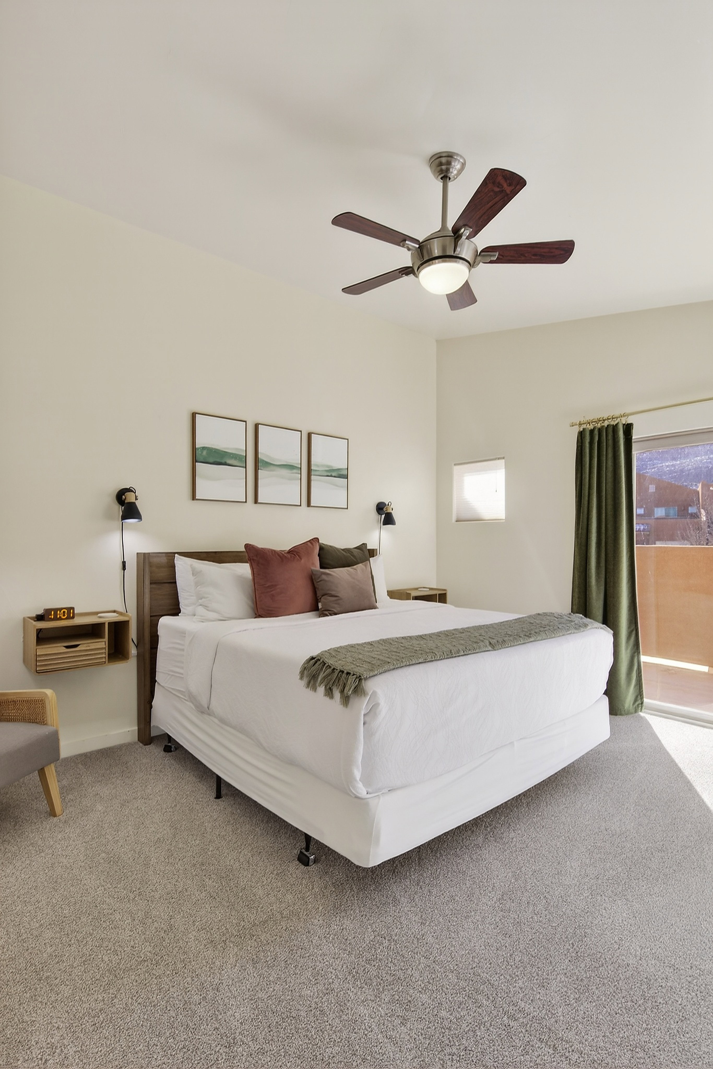 Carpeted bedroom featuring a ceiling fan with integrated lighting, a wooden headboard, wall-mounted sconces, and sliding glass door access