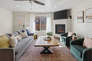 Living area featuring a corner fireplace, recessed lighting, ceiling fan, large window with natural light, and wood-finish flooring