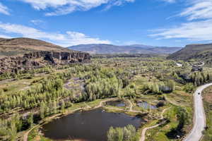 Expansive natural landscape featuring multiple ponds, abundant mature trees, a winding roadway, and distant mountain ranges under a clear sky