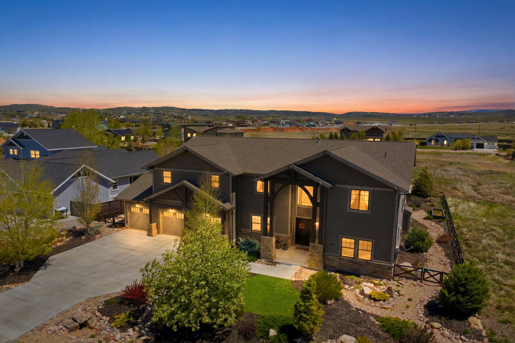 Contemporary two-story residence featuring a dark gray exterior, prominent stone accents, and a covered entryway with exposed wood beams