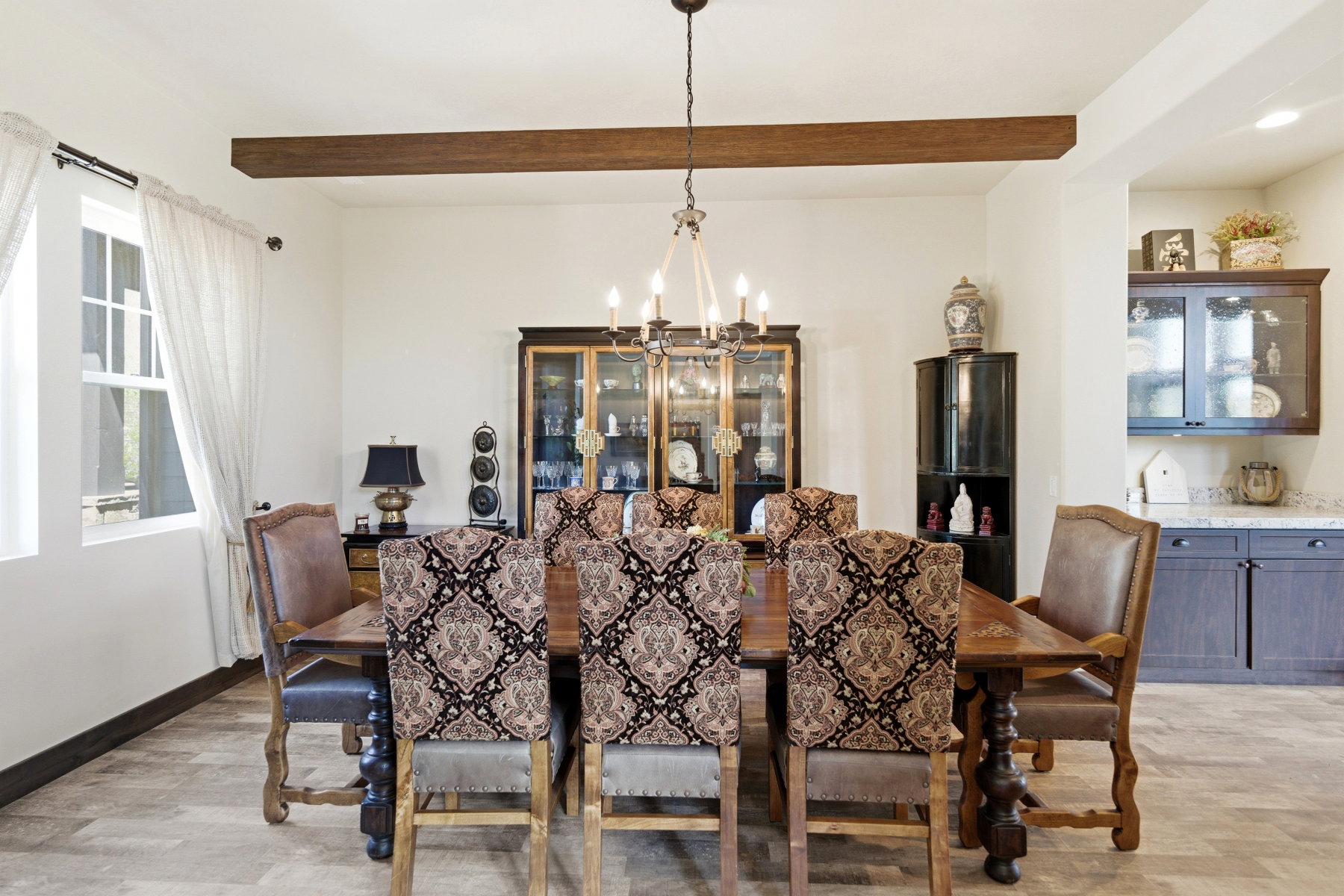 Open dining area featuring a wood-finish beam, central chandelier, and light-toned flooring