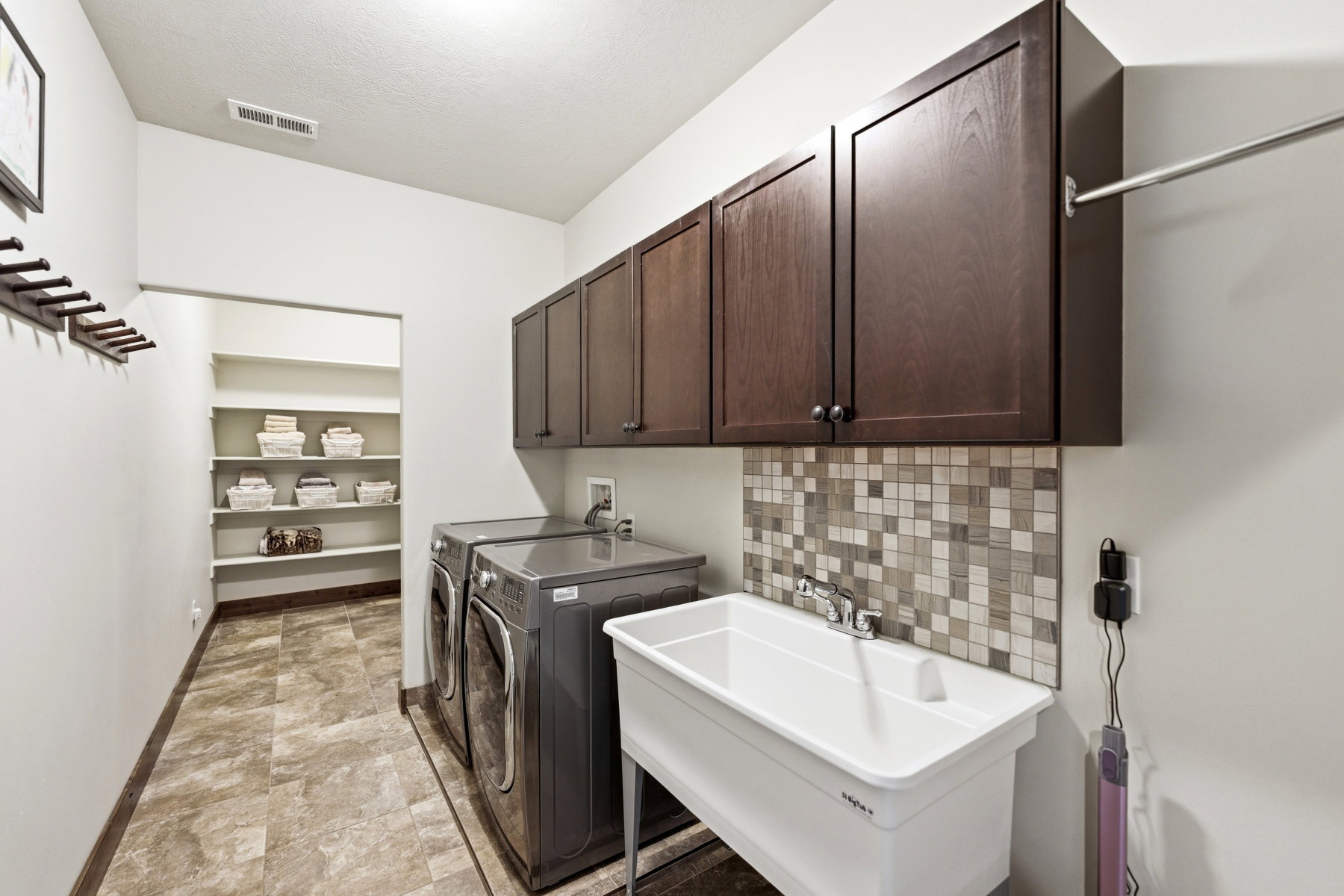 Dedicated laundry space featuring a utility sink with a mosaic tile backsplash, dark wood-finish cabinetry, and an integrated clothing rod