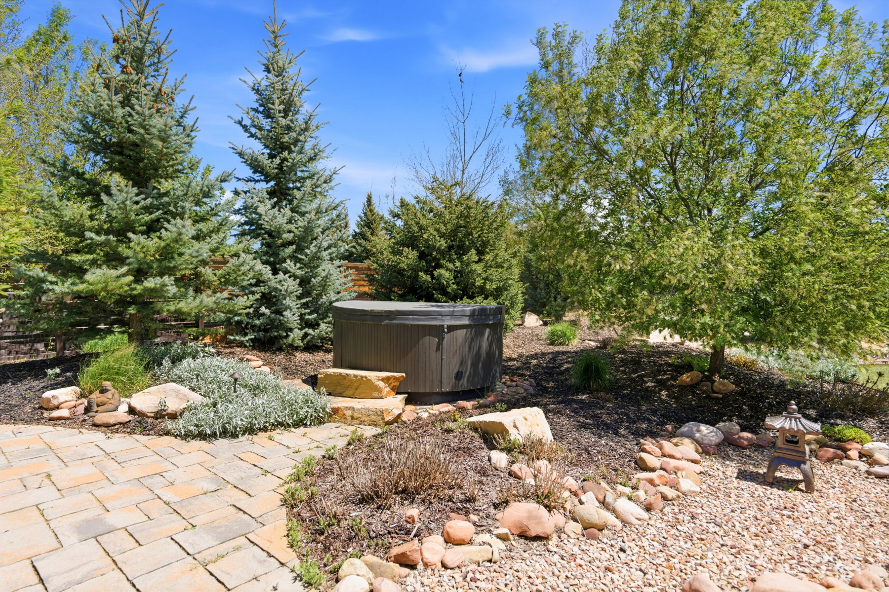 Private outdoor spa area featuring a circular hot tub with stone steps, surrounded by mature evergreen trees