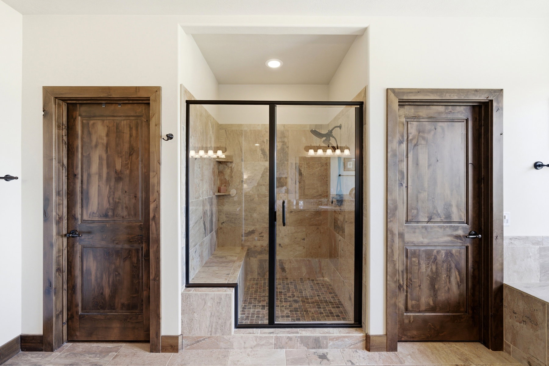 Frameless glass shower enclosure featuring a tiled bench, recessed niche, and mosaic tile flooring