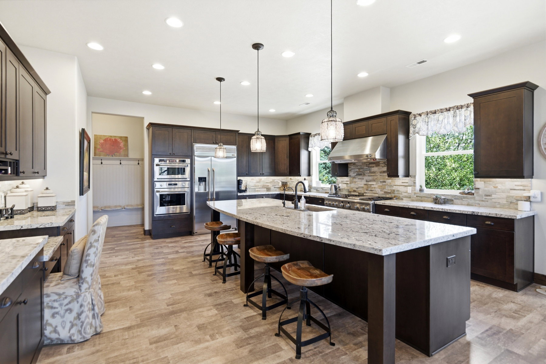 Spacious kitchen featuring an expansive center island with seating, dark wood cabinetry, light stone countertops, stainless steel appliances, and wood-finish flooring