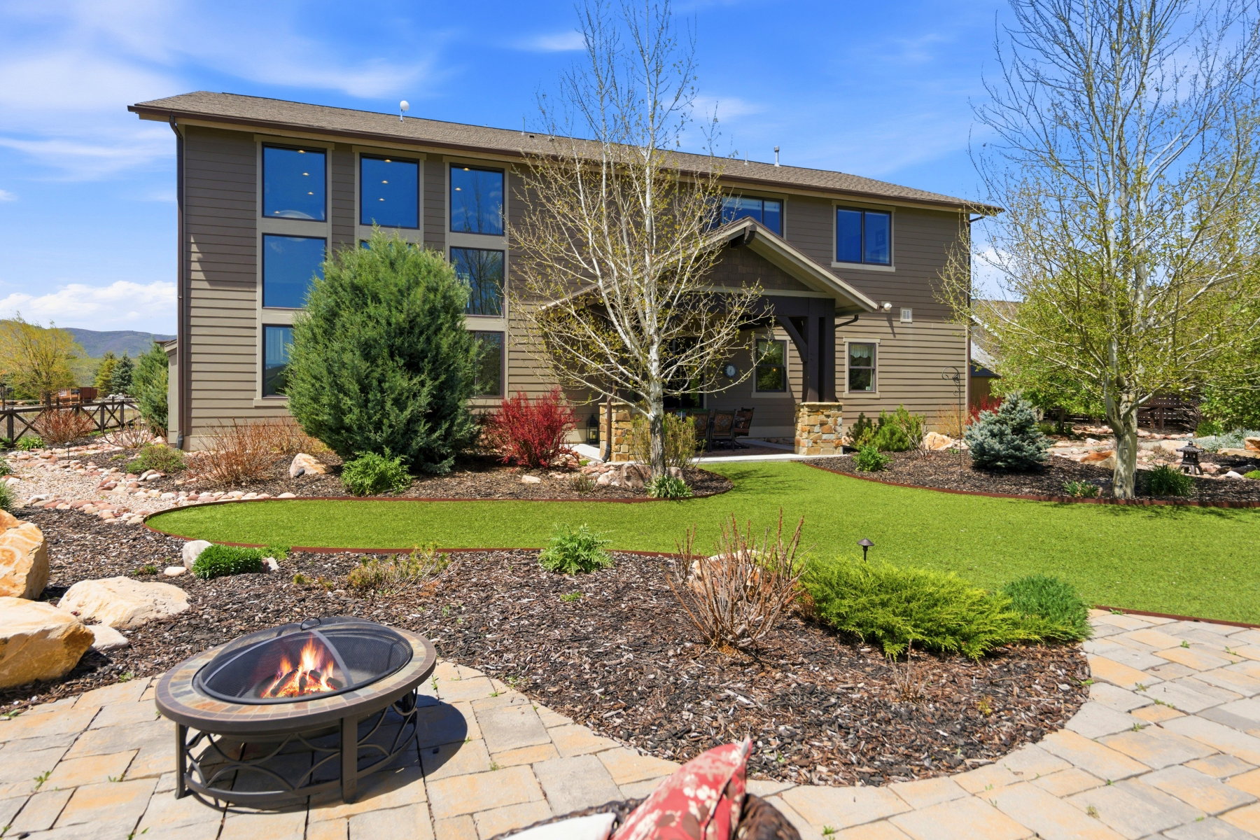 Expansive backyard featuring a manicured lawn, established landscaping, and a paver patio with a fire pit