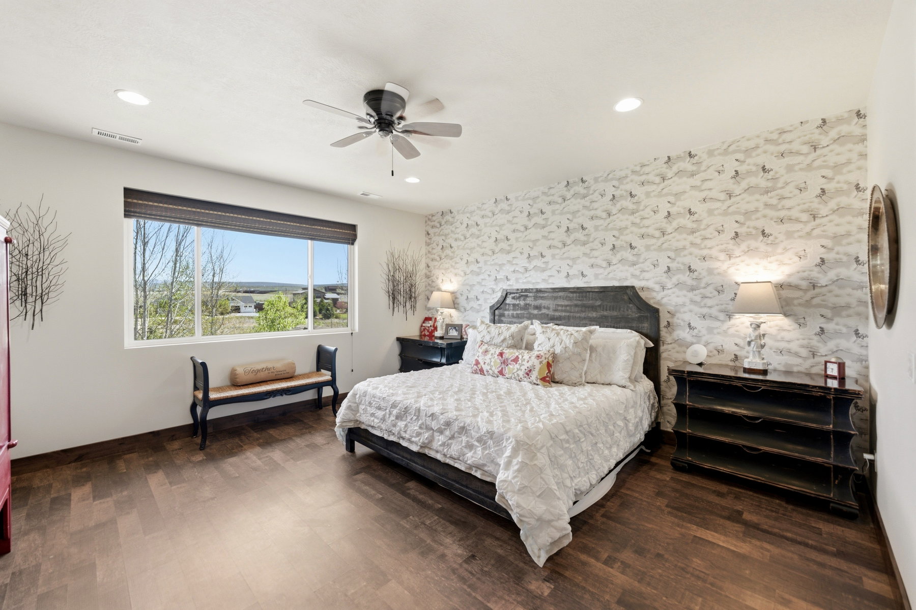 Spacious room featuring wood-finish flooring, a wide window with a dark Roman shade, and a textured accent wall
