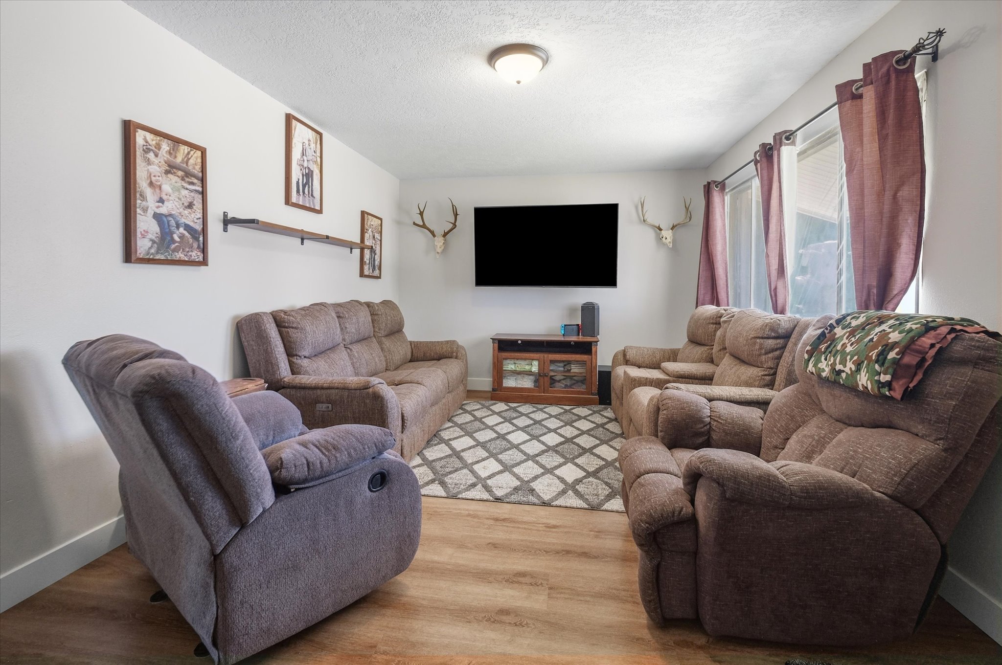Living area featuring wood-finish flooring, light-colored walls, recessed ceiling lighting, and a window with drapes