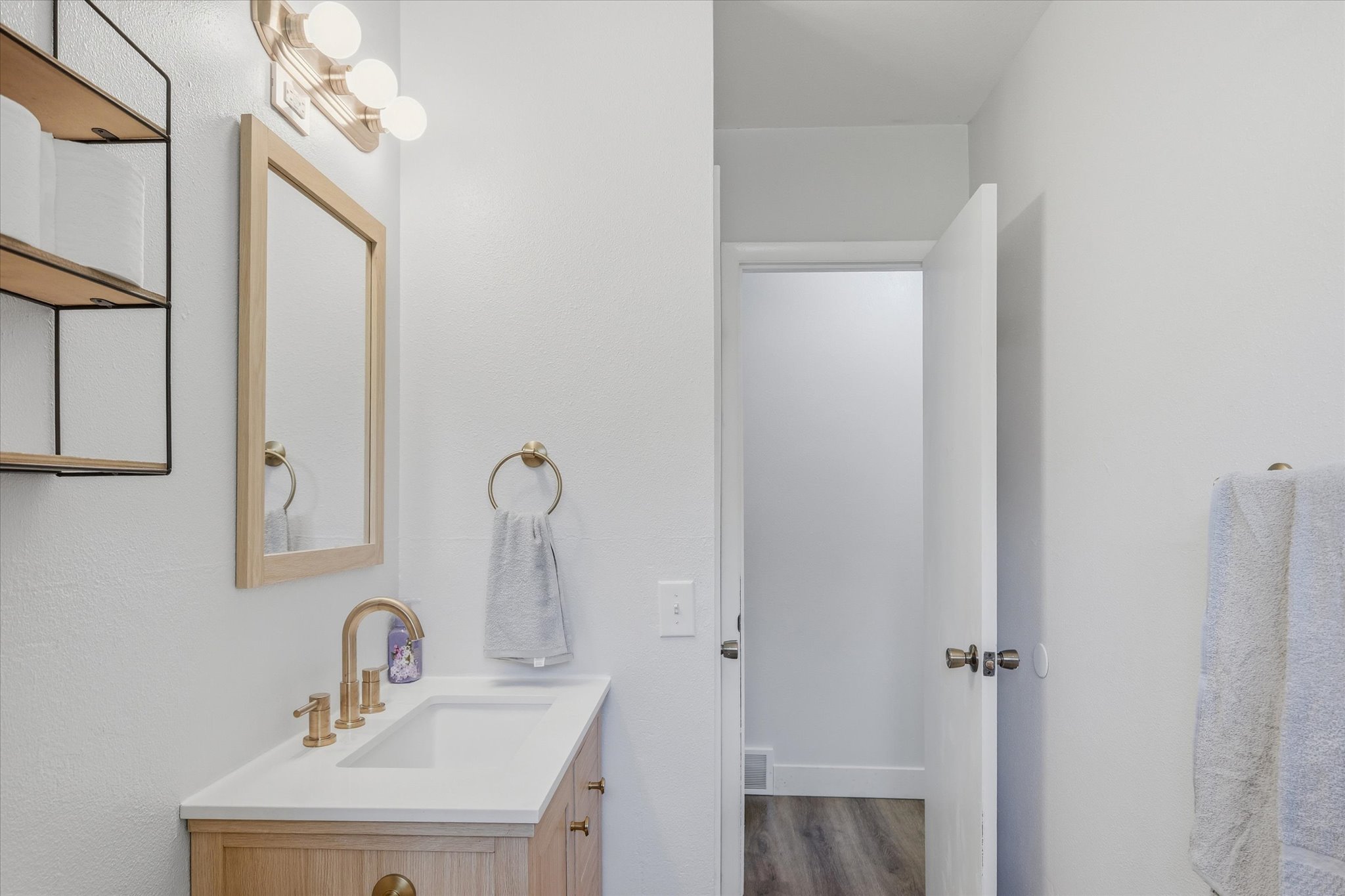 Bathroom vanity featuring a light wood-finish cabinet with brass hardware, a white integrated sink, and a brass-finish faucet