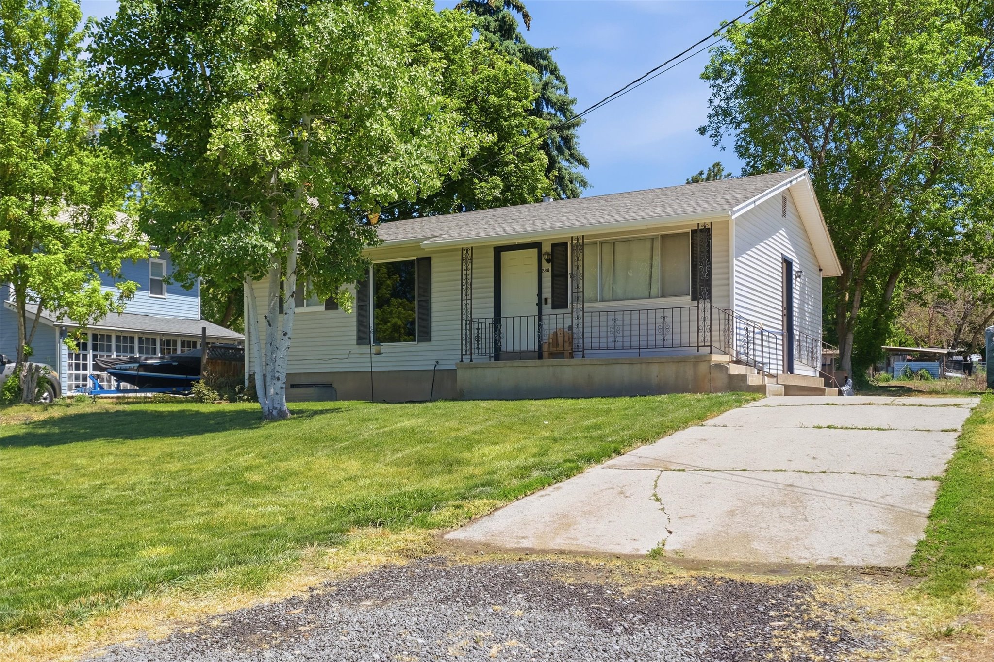 White siding exterior with a pitched roof, front porch with wrought iron railing, and a concrete driveway