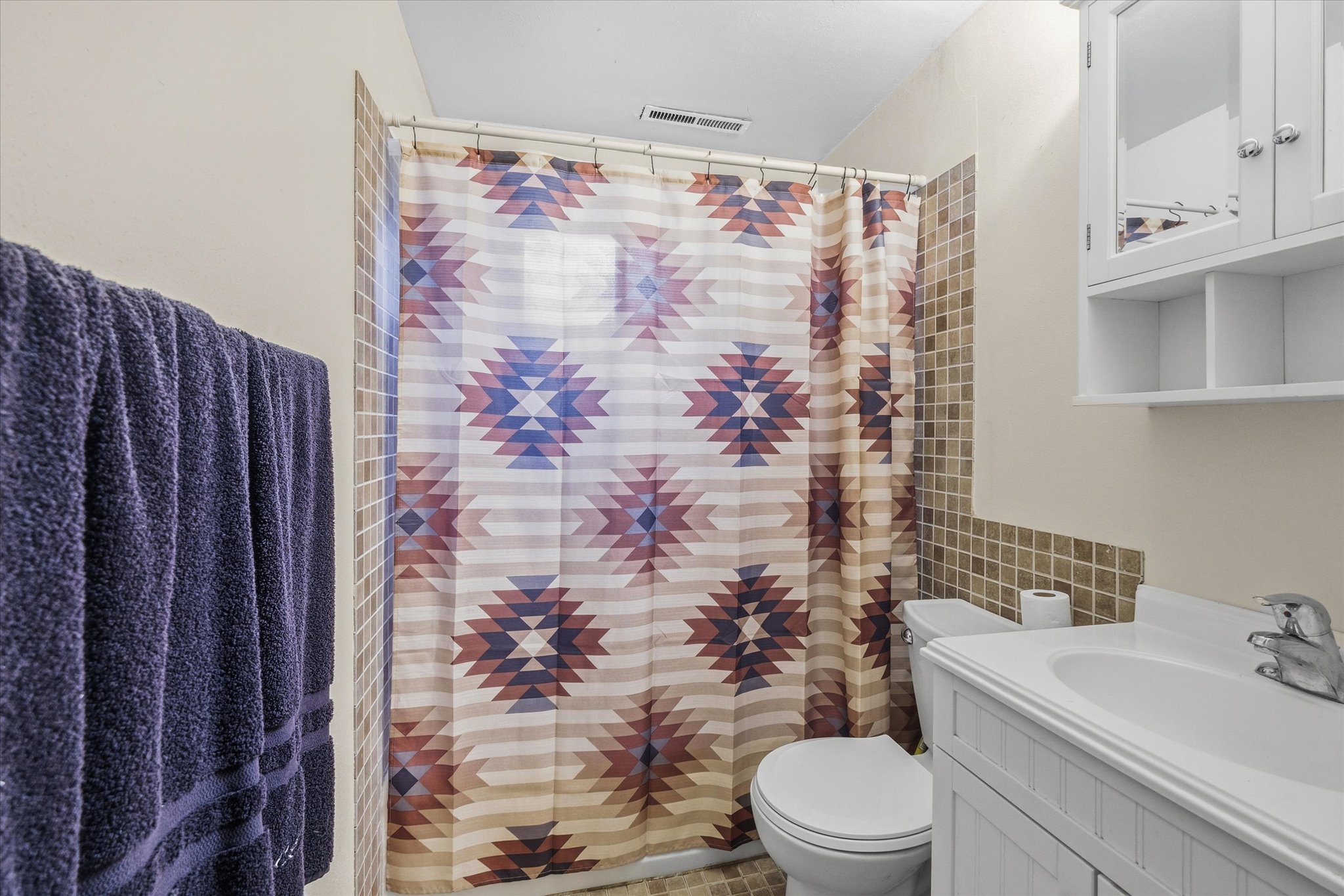 Bathroom featuring a tiled shower surround, white vanity with integrated sink, chrome faucet, and a wall-mounted medicine cabinet with open shelving