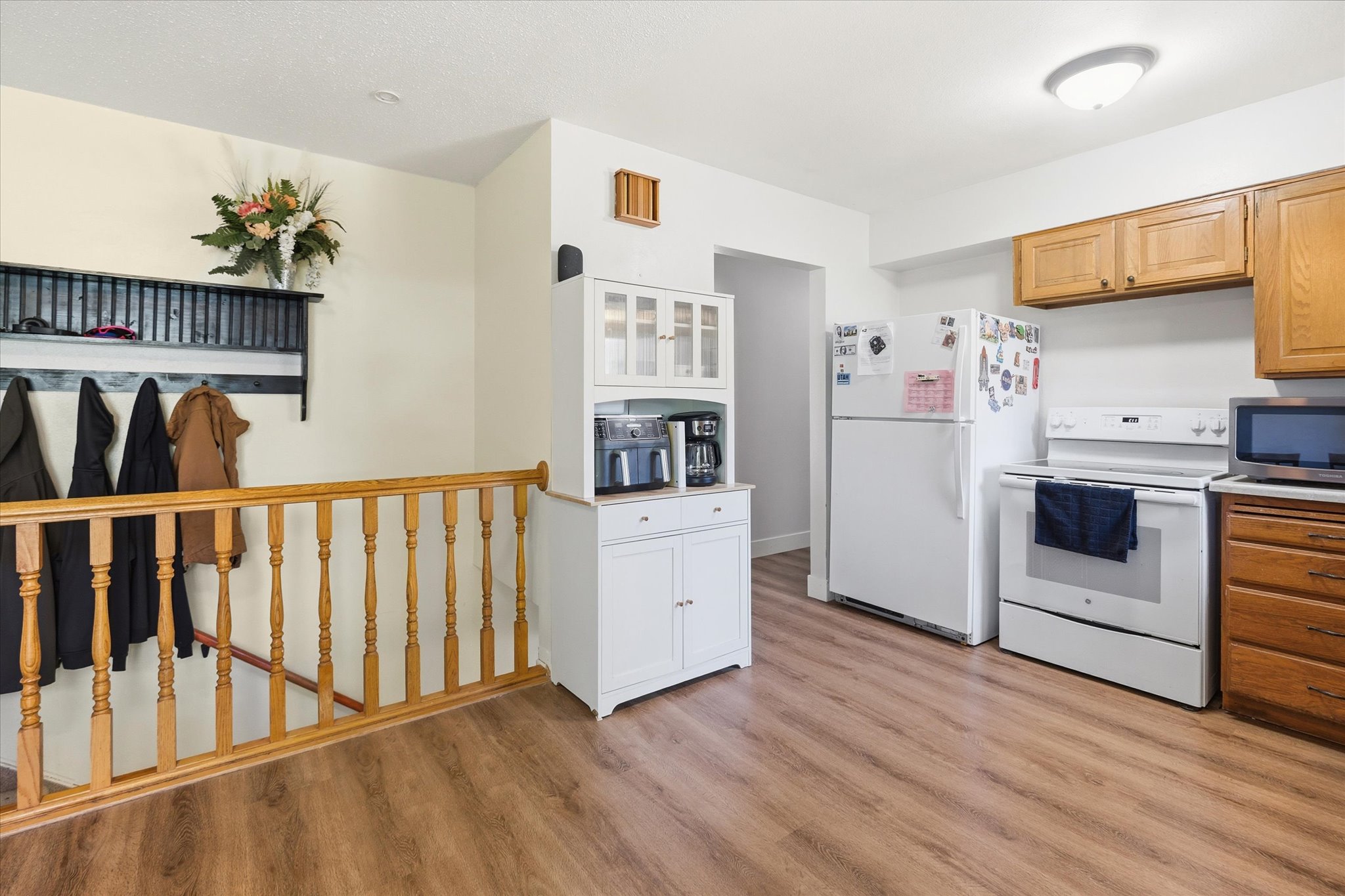 Kitchen area featuring wood-finish flooring, white appliances, and a combination of wood and white cabinetry
