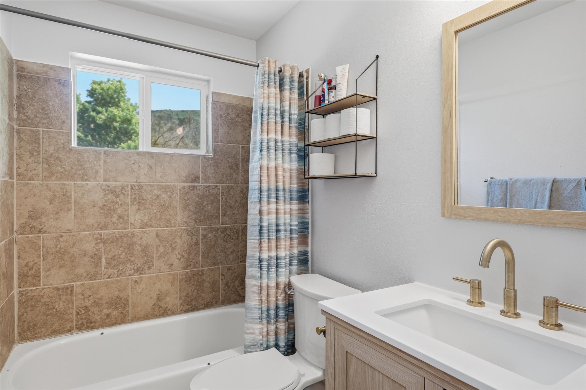 Modern bathroom featuring a single vanity with wood-finish cabinetry, a rectangular undermount sink, and a gold-tone faucet