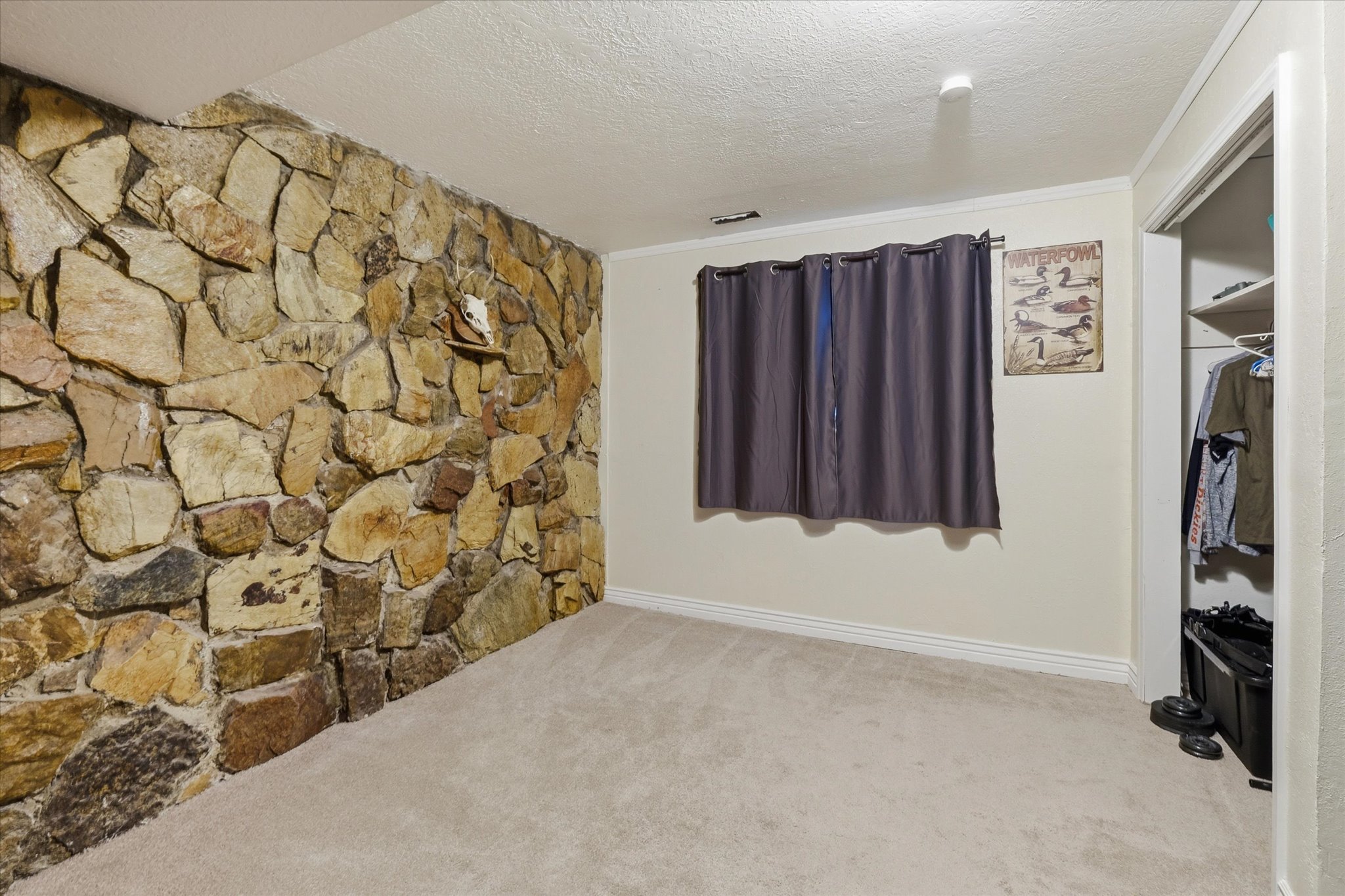 Accent stone wall featuring natural rock, neutral-toned carpeting, white baseboards, a window with dark curtains, and a built-in closet with shelving