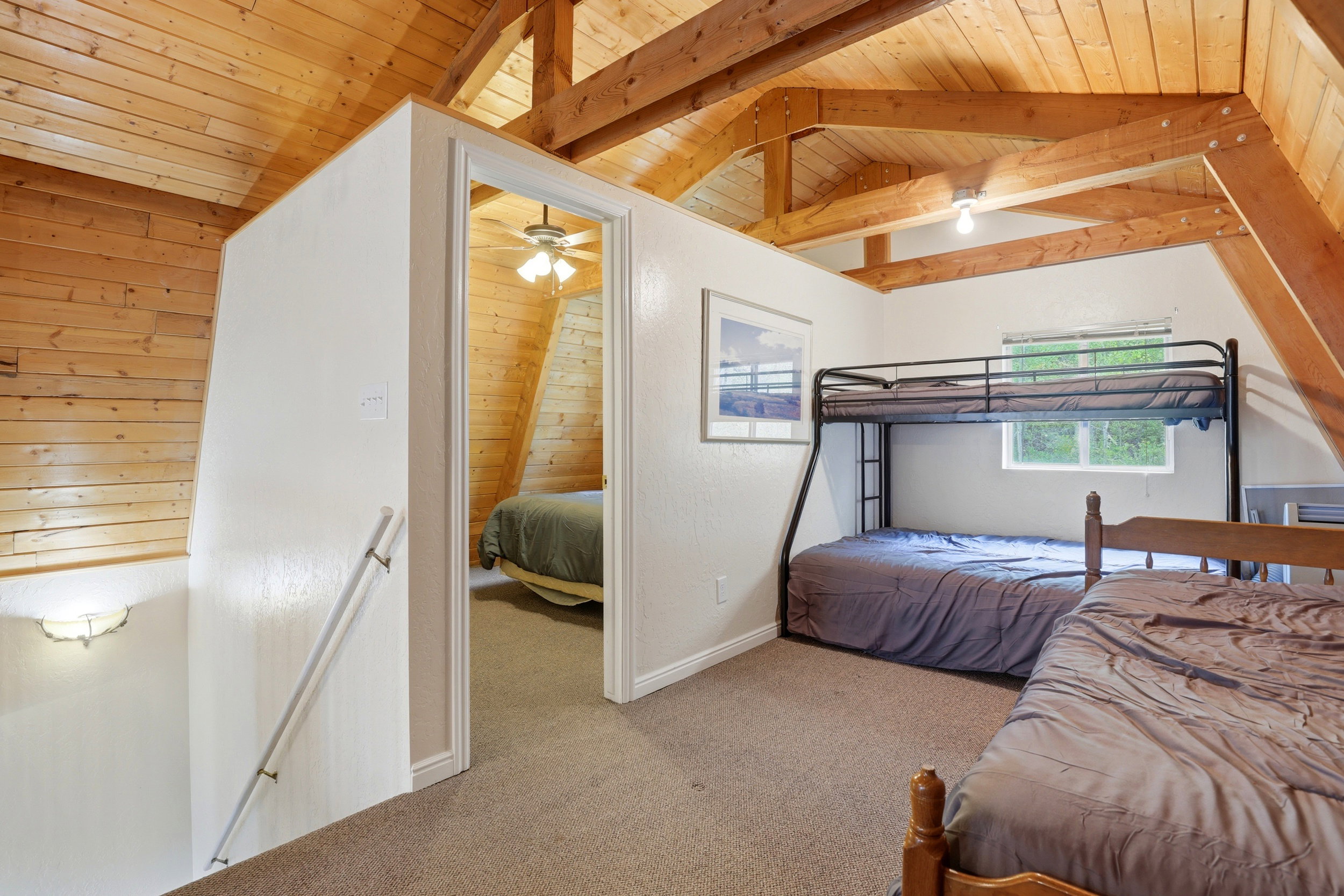 Carpeted loft area featuring exposed wood beams, a window, and a doorway opening to an additional room