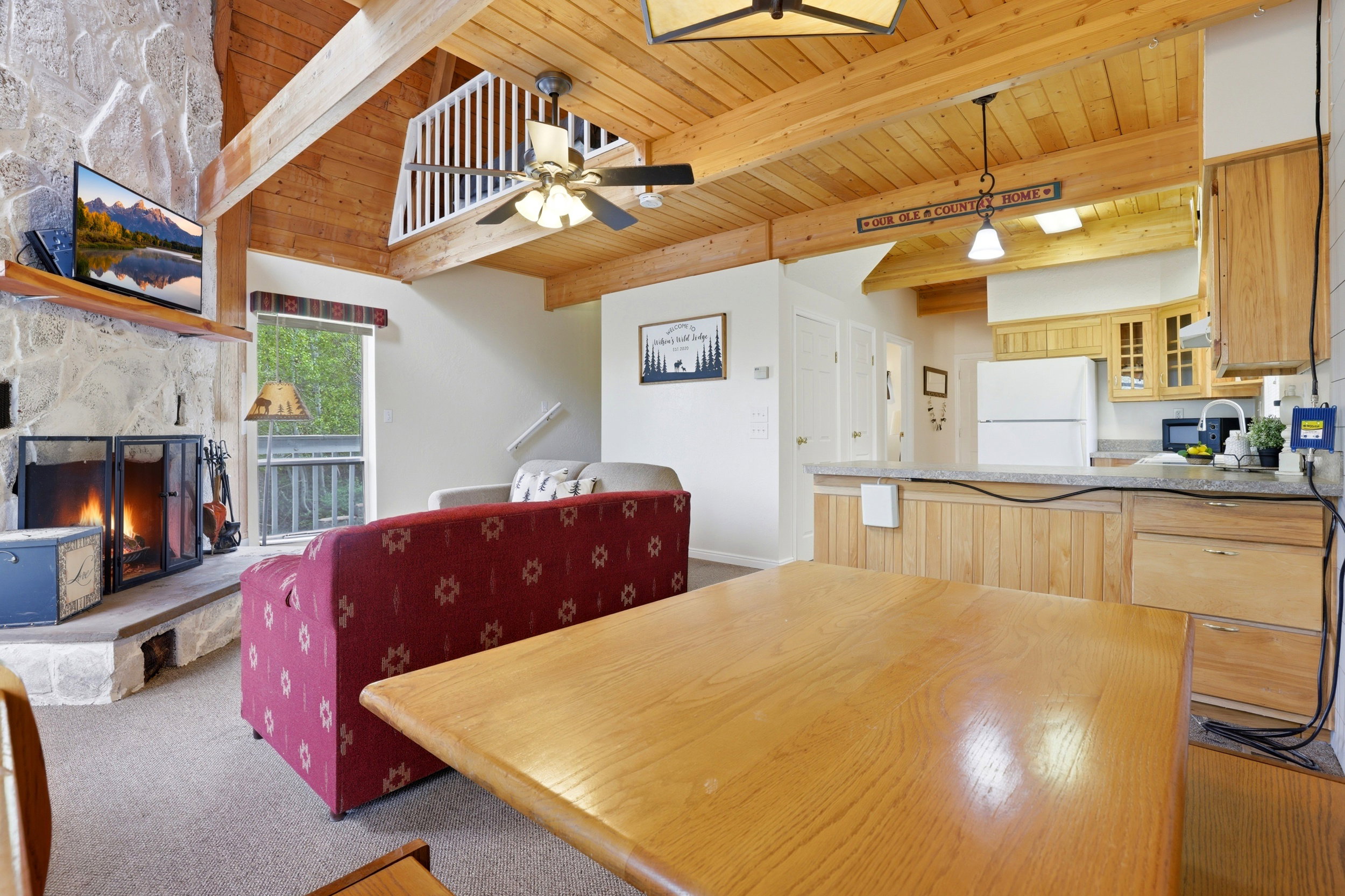 Vaulted wood-paneled ceilings with exposed beams, a stone-faced fireplace, a kitchen island with beadboard paneling, and wood-finish flooring