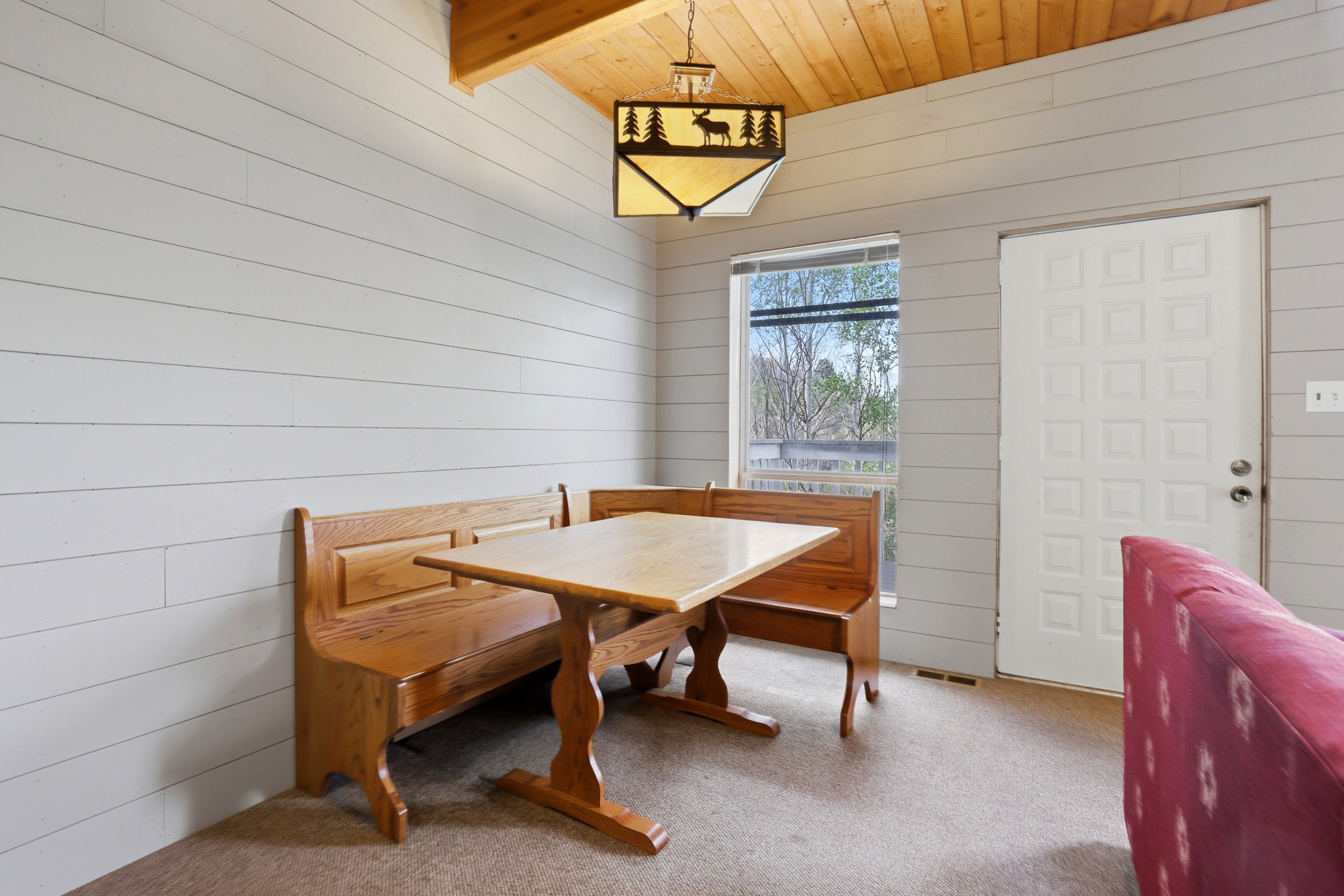 Vaulted wood-paneled ceiling with a decorative pendant light fixture, shiplap-style walls, carpeted flooring, and a window providing natural illumination