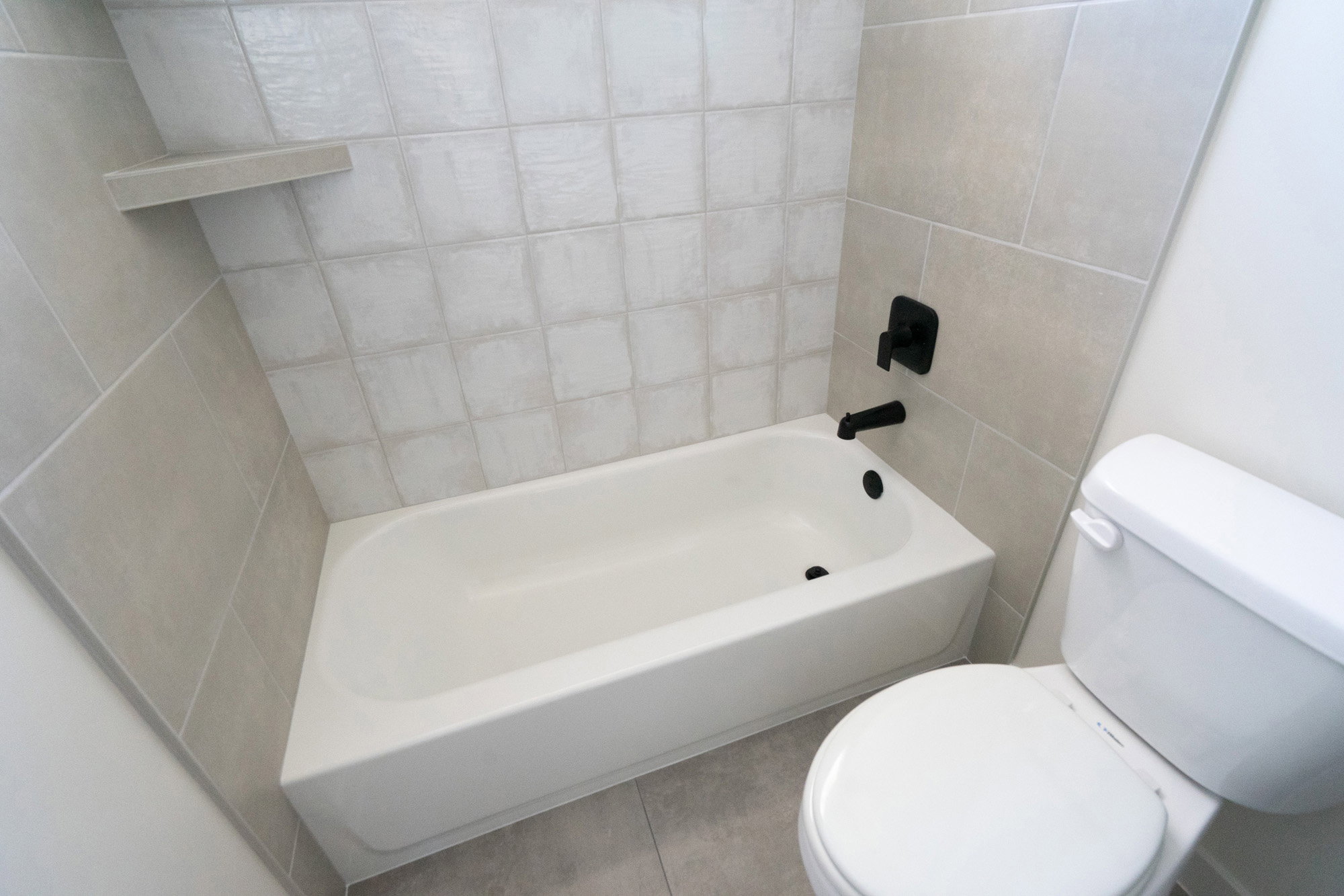 Tub and shower combination featuring black fixtures and light-colored tile surround