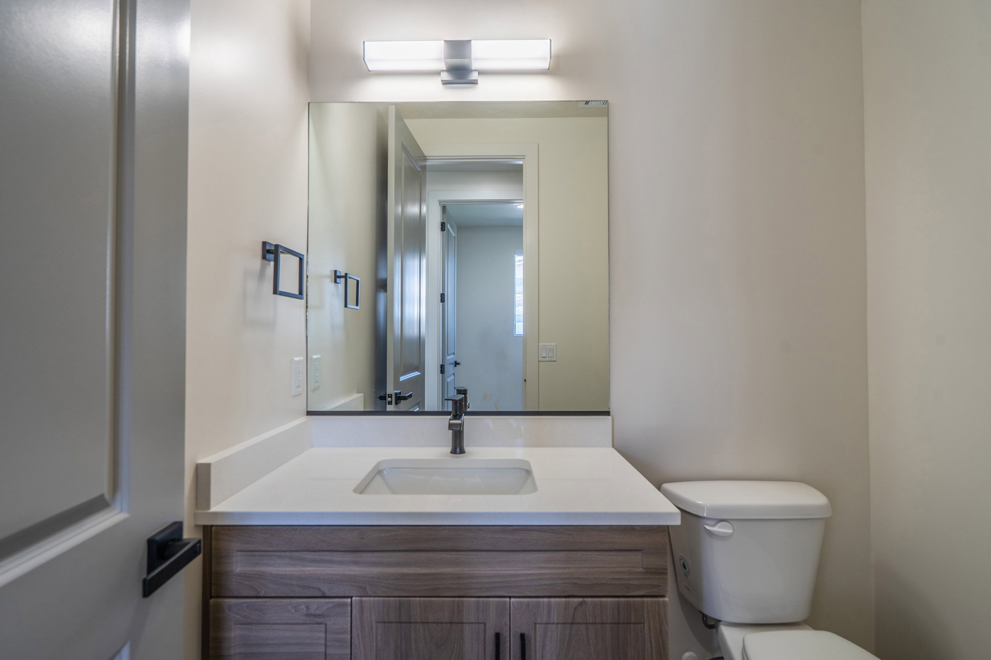 Modern vanity featuring a rectangular undermount sink, a white countertop, and wood-finish cabinetry with dark hardware