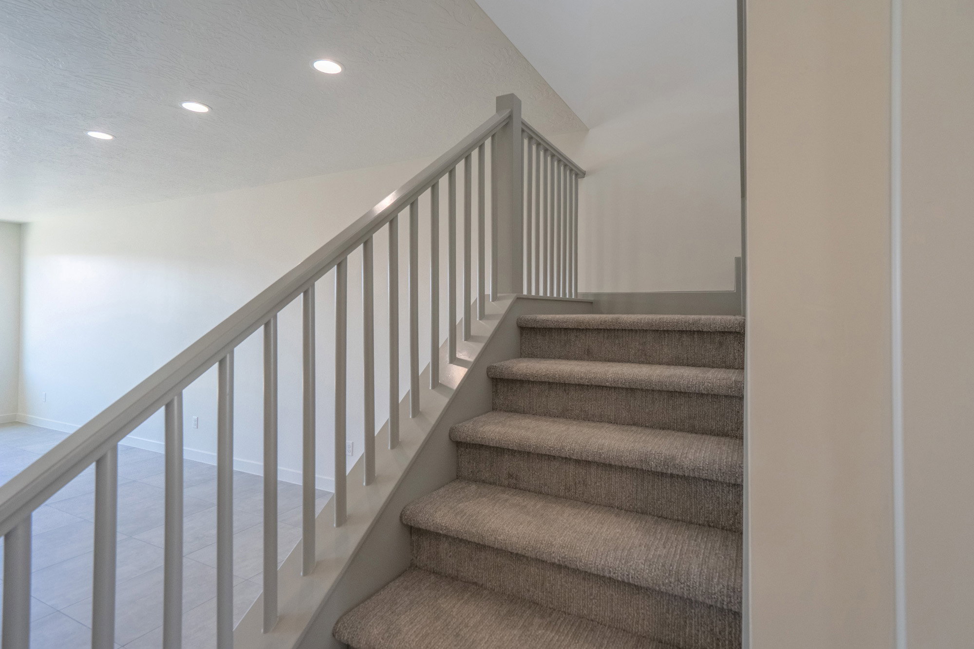 Carpeted staircase with light gray balusters and handrail, featuring recessed lighting in the ceiling above