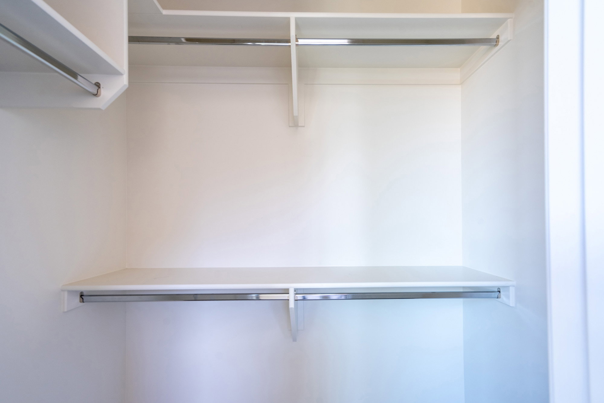 White built-in closet system featuring multiple shelves and chrome hanging rods