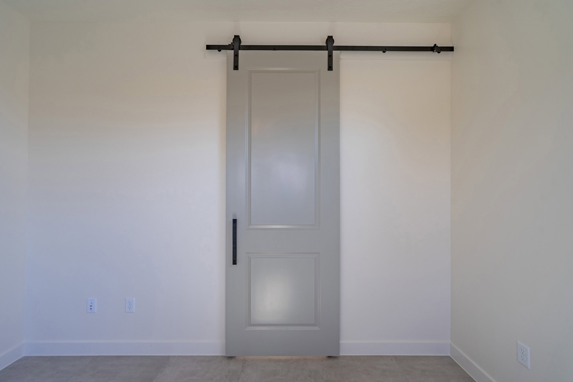 Light gray paneled barn door with a matte black track and handle