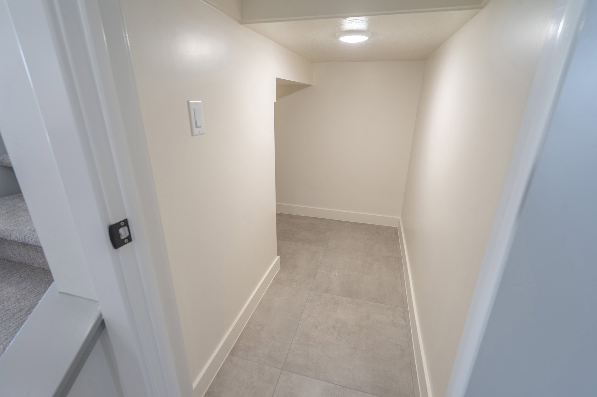 Lower-level hallway featuring light gray tile flooring, crisp white baseboards, and neutral wall paint