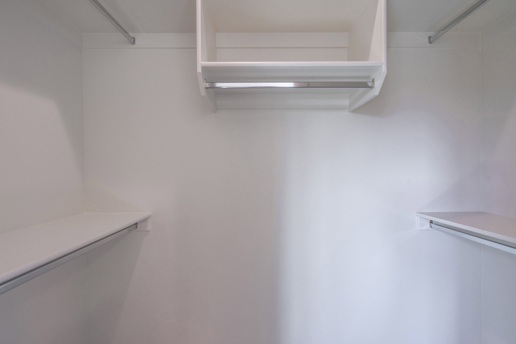 Spacious white-painted closet with multiple shelving units and chrome hanging rods