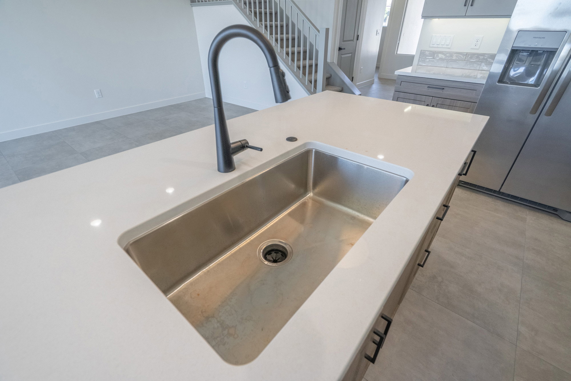 Kitchen island with a large undermount stainless steel sink, a matte black gooseneck faucet, light-toned countertops, and integrated cabinetry