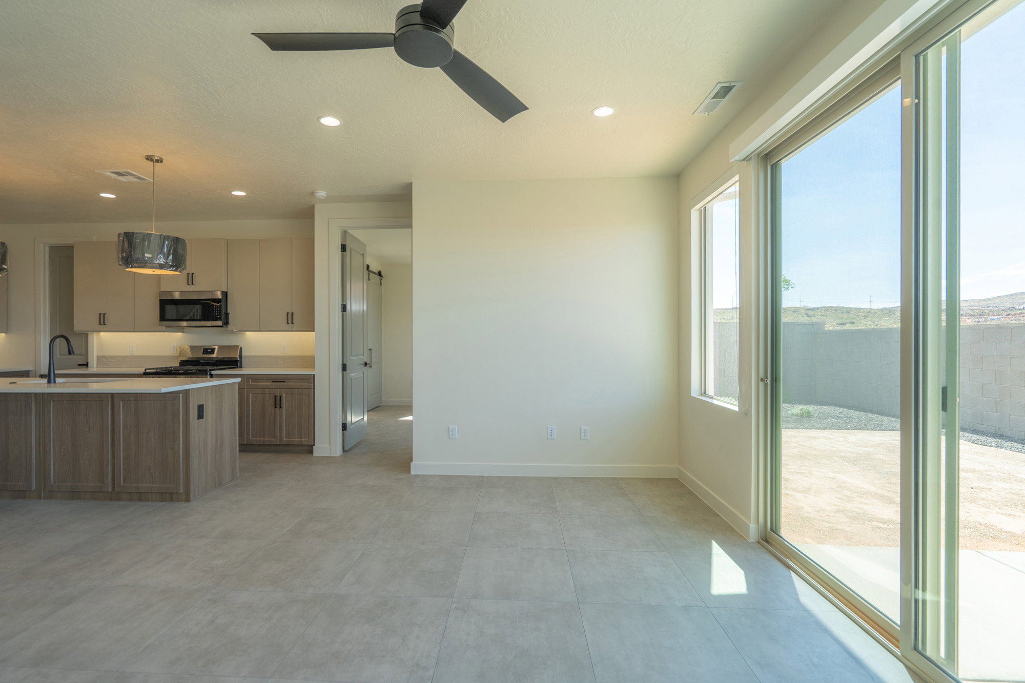Open-concept interior featuring light gray tile flooring, a modern kitchen with a large island and stainless steel appliances, recessed lighting, and a ceiling fan