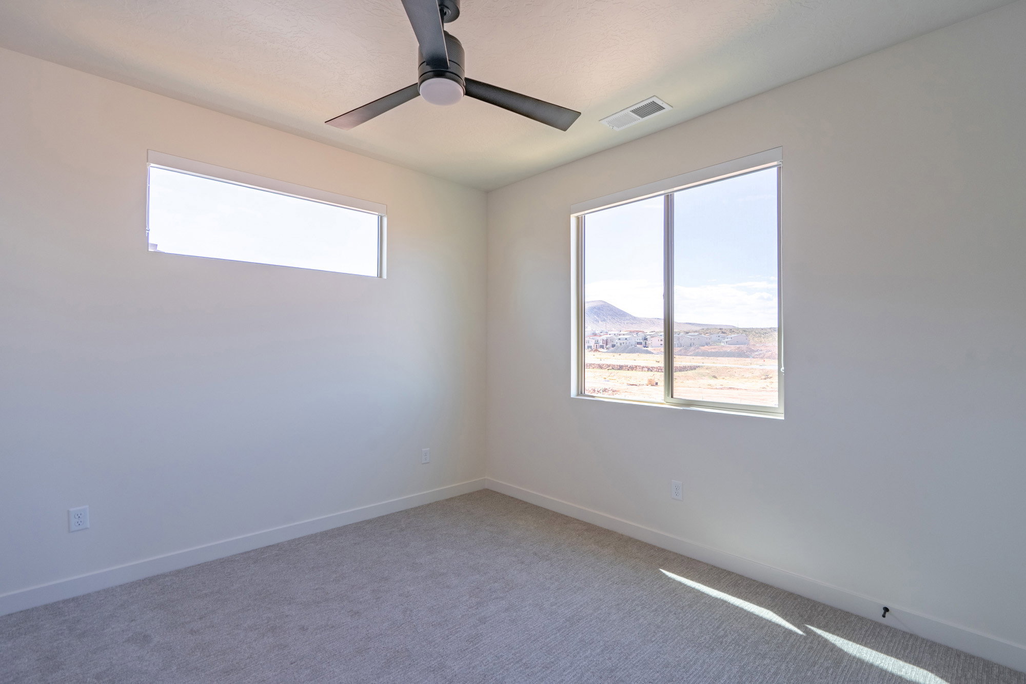 Light-filled room featuring a broad window, a horizontal transom window, a ceiling fan, and light gray carpeting