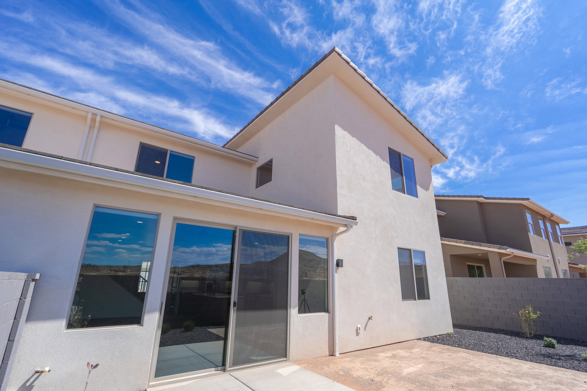 Rear exterior featuring a sliding glass door, multiple windows, a concrete patio, and a low-maintenance landscape with dark aggregate