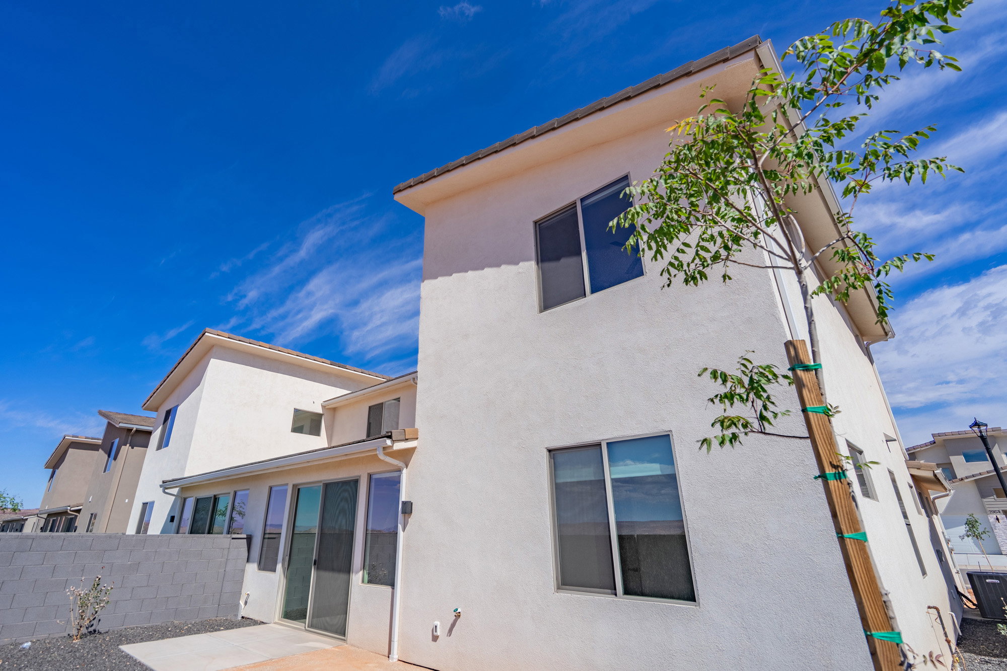 Stucco exterior with multiple windows, a concrete patio, and a block wall perimeter