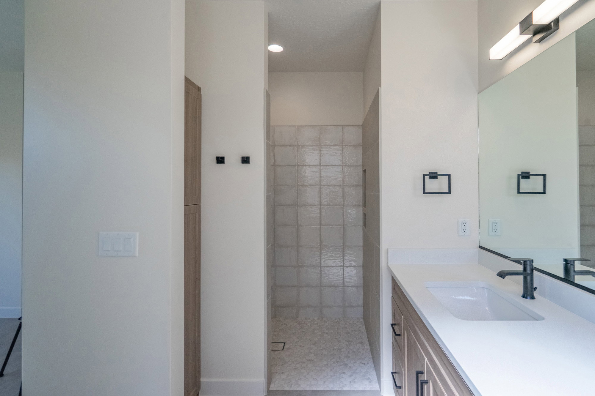 Shower stall with light-toned square wall tiles and a pebble-finish floor