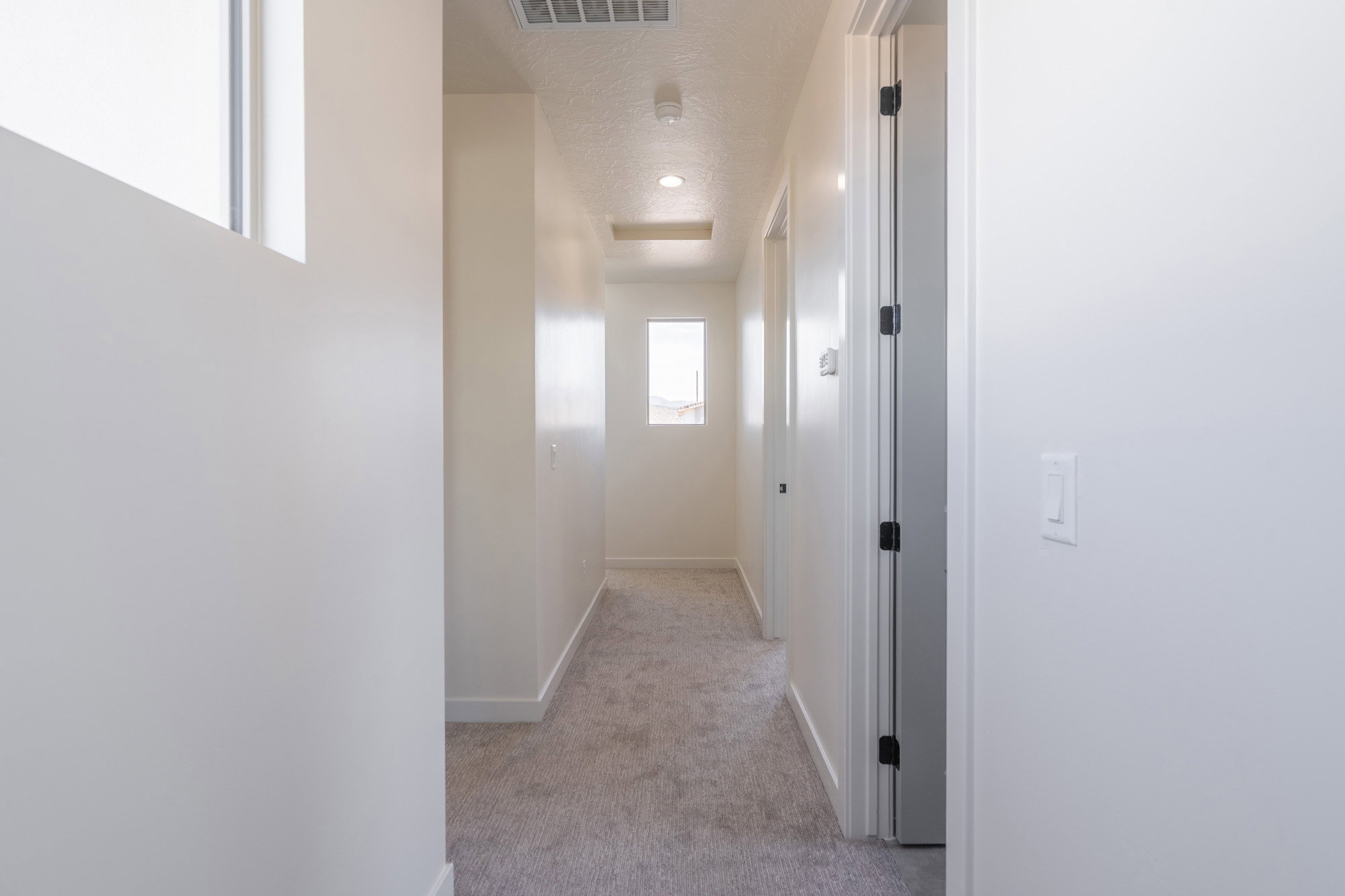 Carpeted hallway featuring bright white walls, recessed lighting, and natural light from multiple windows