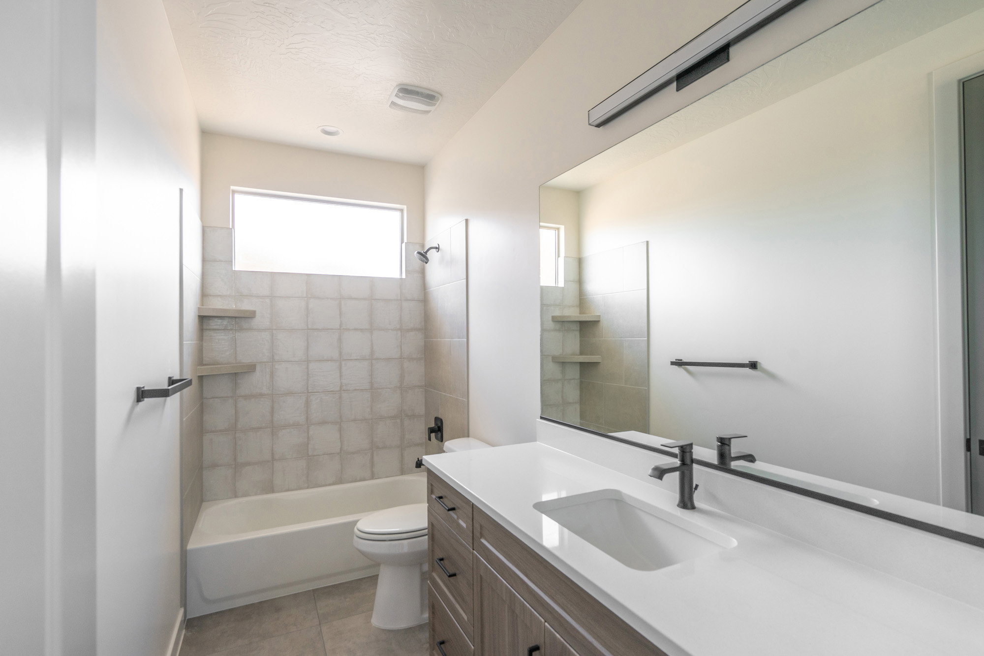 Bathroom featuring a single vanity with an integrated sink, matte black faucet, and a large mirror with linear overhead lighting